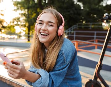 Positive young teenage girl outside in park holding mobile phone.