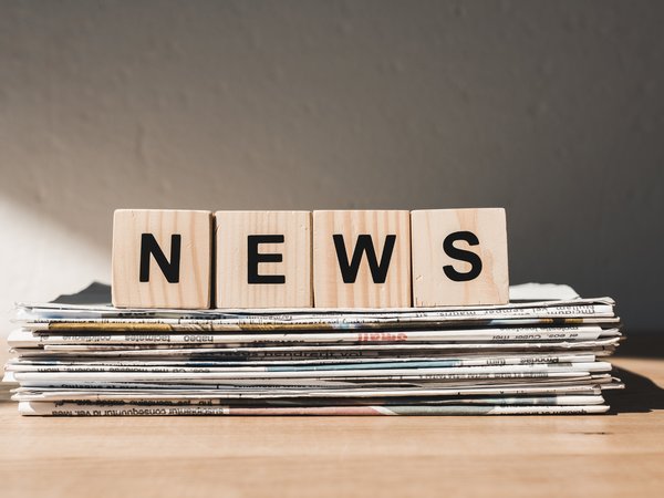 Holzwürfel mit der Aufschrift NEWS auf einem Stapel Papierzeitungen