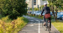 Stylish businessman in helmet cycling on bike path in sunny day.