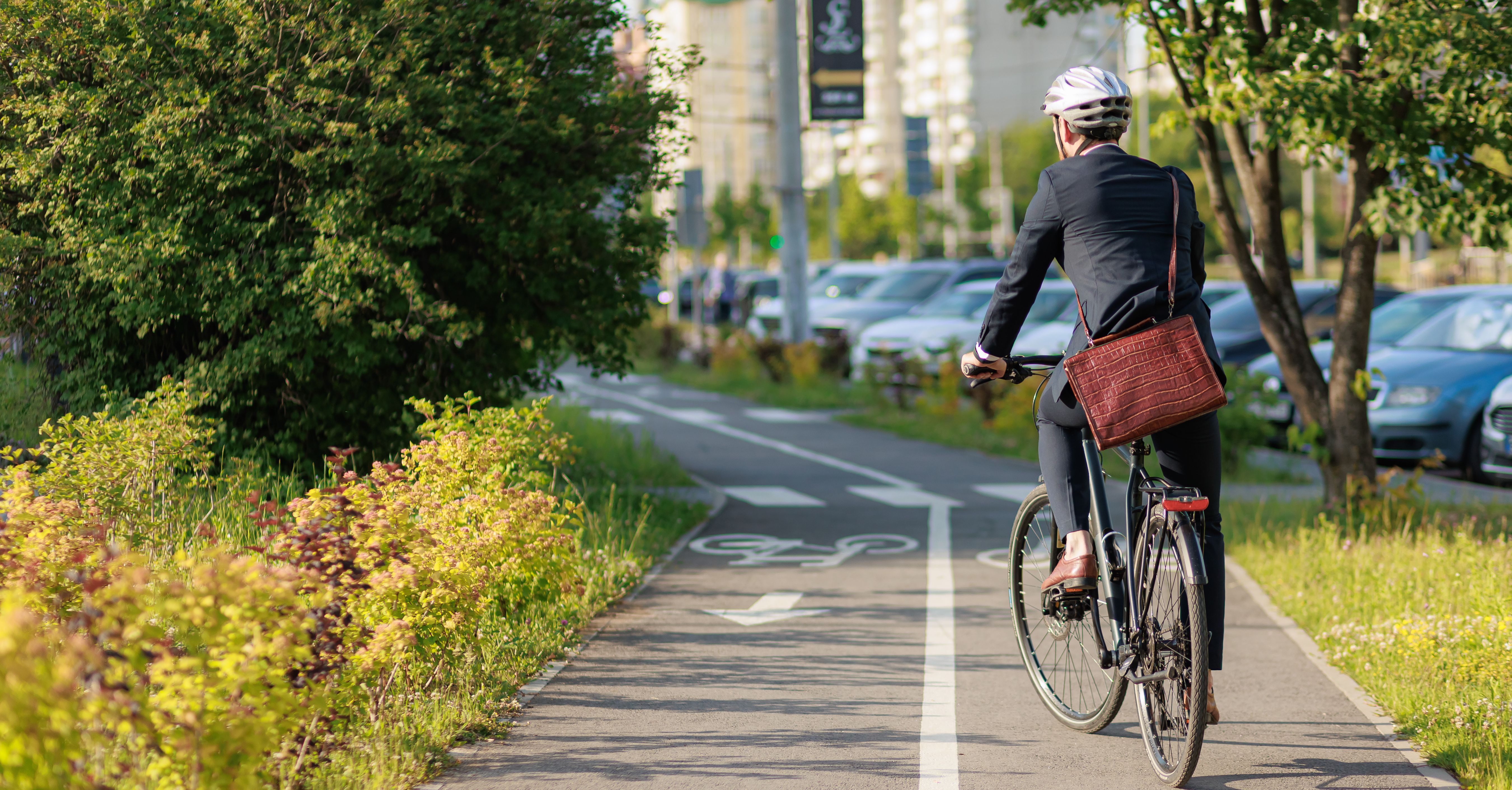 Stylish businessman in helmet cycling on bike path in sunny day.