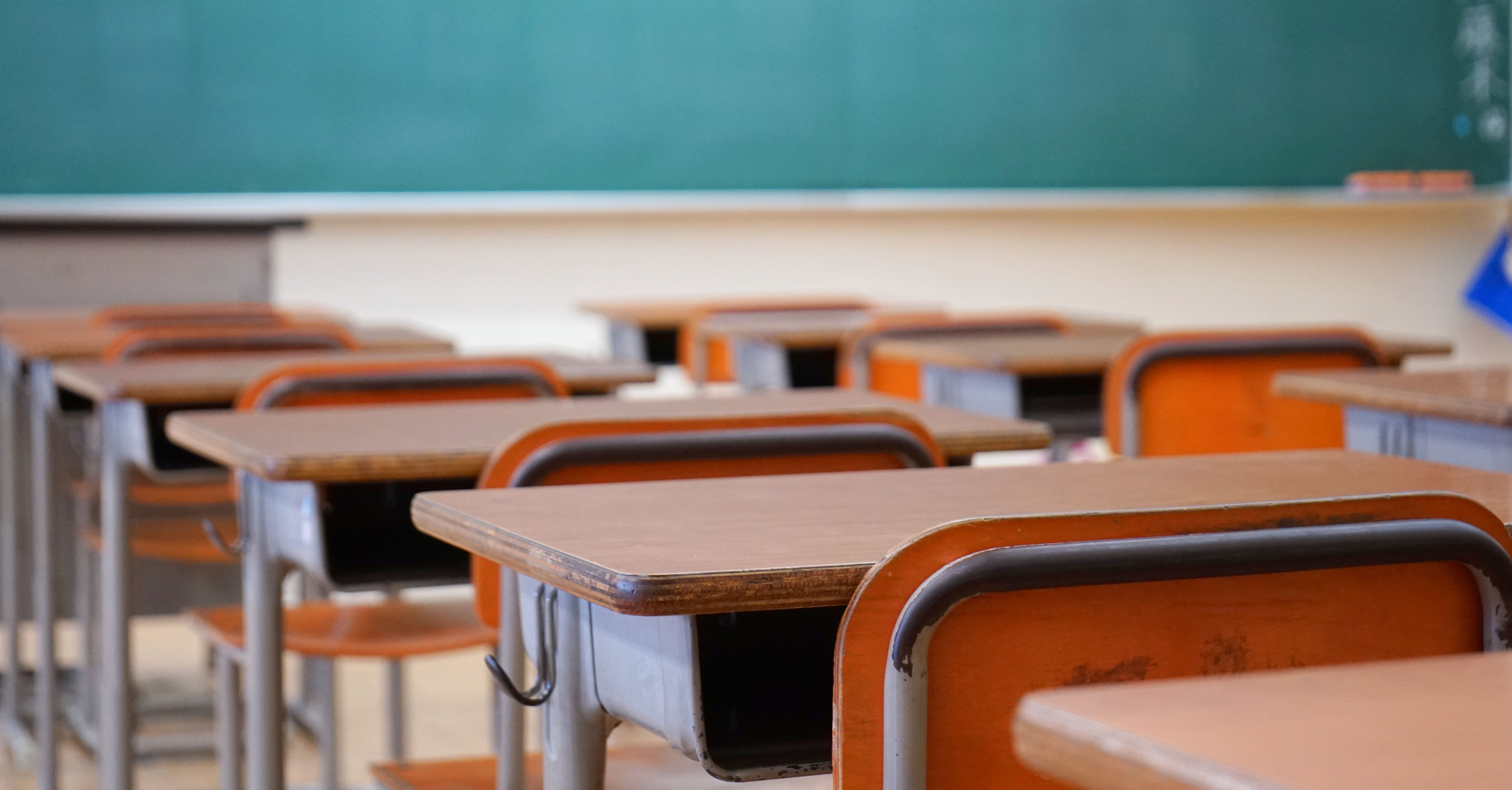 Schulbänke in einem Klassenraum mit einer Tafel im Hintergrund
